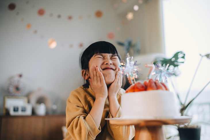 A happy and excited young Asian girl showing excitement with her birthday cake. She is enjoying her birthday celebrations in a decorated home environment.