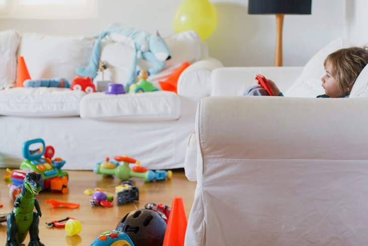 Colorful chaos fills a cozy living room as a young child looking a digital tablet