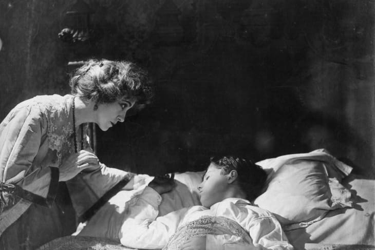 1921: American actress Florence Turner (1887 - 1946) leans over the bed of a sleeping boy, in a screen adaptation of Arnold Bennett's book, 'The Old Wives' Tale', directed by Denison Clift for Ideal.