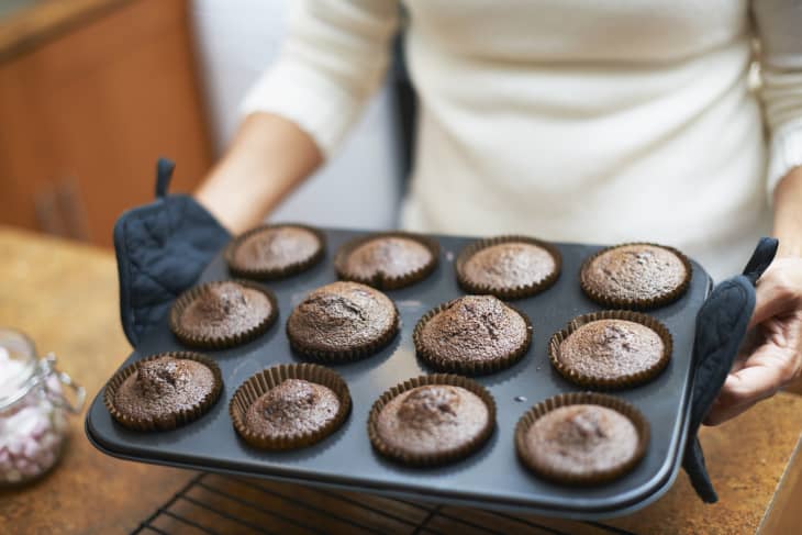 Womans hands lifting cup cake baking tray onto kitchen counter