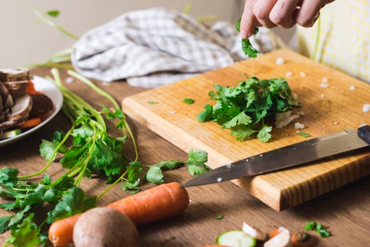 Cropped Image Of Person Chopping Cilantro On Cutting Board.