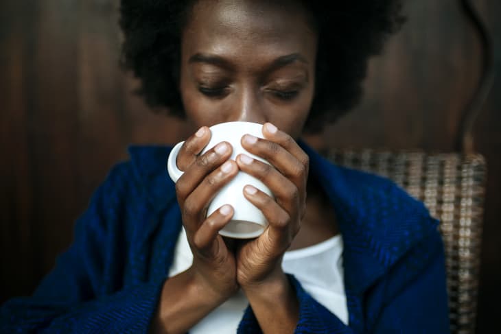 Black woman drinking coffee from a mug she's holding with both hands