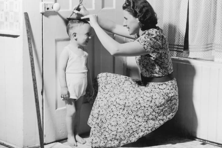 A mother marks her son's height on the door with a pencil, circa 1950.