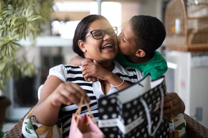 mom being kissed and hugged by her kid while opening a gift bag
