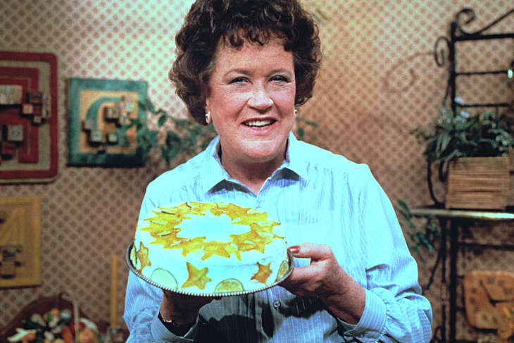 Julia Child in her kitchen with a cake in hand.