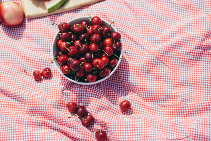 A bowl of cherries on a red gingham blanket
