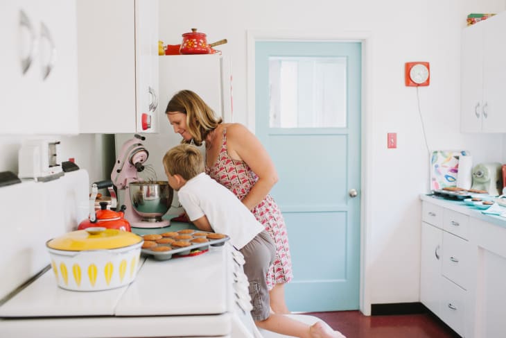 Woman and child baking in a retro kitchen with a pink mixer, muffins on the counter, and colorful cookware.