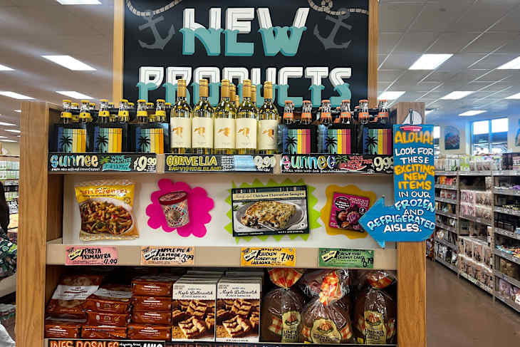 Display of new grocery products featuring wine, pasta, desserts, and a sign directing to frozen items.