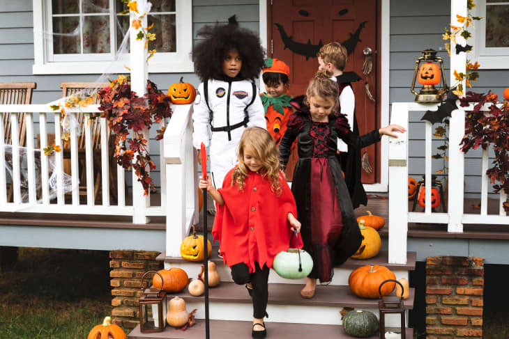 Children in Halloween costumes on porch steps with pumpkins and autumn decor.