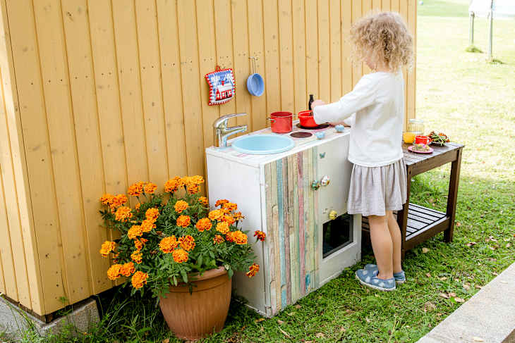 Young girl child playing outdoors in so called mud kitchen, where you can make fake food, play with sand, dirt, water, plants and make a mess, it develops imagination and exploration.