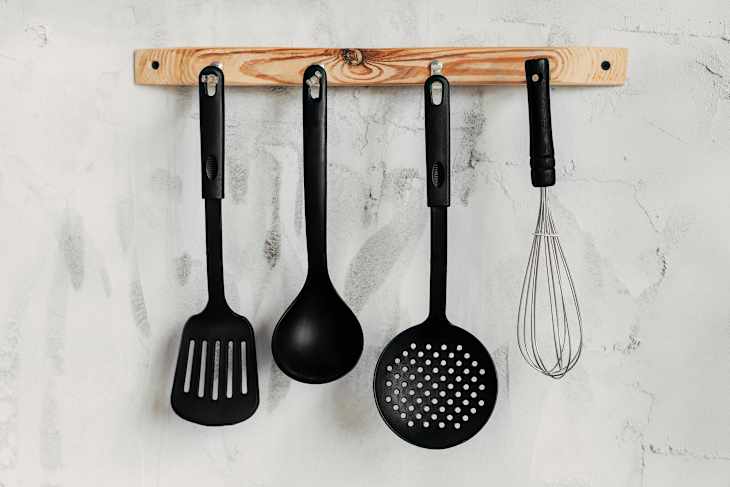 Black kitchen utensils against the background of a light texture wall. Kitchen wallpapers