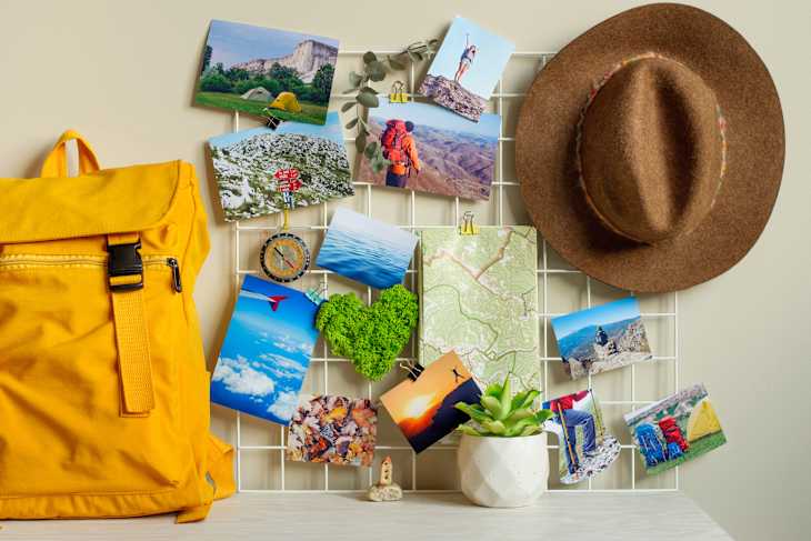 Travel hipster mood board with printed photographs, map, compass, green moss heart and hat on the wall near backpack and succulent on the table.