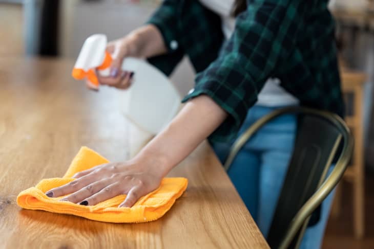 Close up view of happy woman clean home or restaurant. She wiping dust using spray and orange fabric cleaning on dirty table. House keeping maid cleaning service job to prevent covid19 virus outbreak.