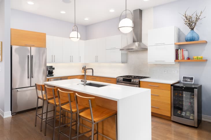 ELMHURST, IL, USA - JULY 12, 2021: A luxury kitchen with a waterfall granite island, wood and white cabinets, stainless steel appliances, and hardwood flooring