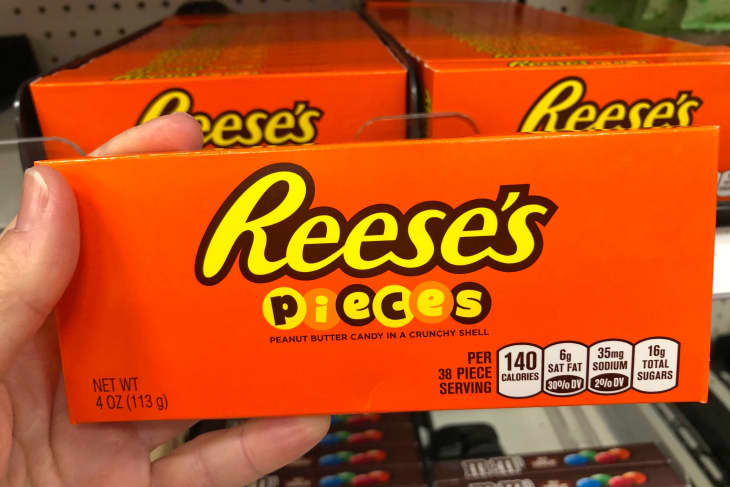 Hand holding a box of Reese's Pieces candy with store shelf in background.