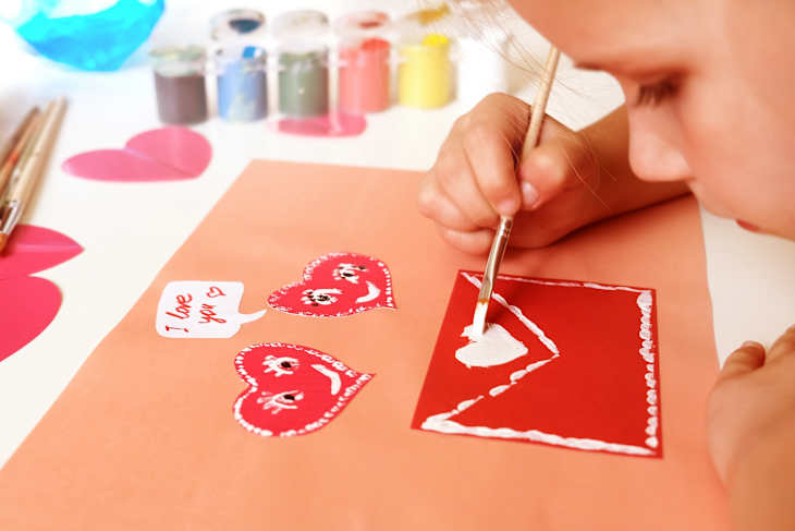 Child created homemade greeting card. A little girl painted and colored card with funny hearts. Gift for Mothers Day or Valentines day. Arts and crafts concept.