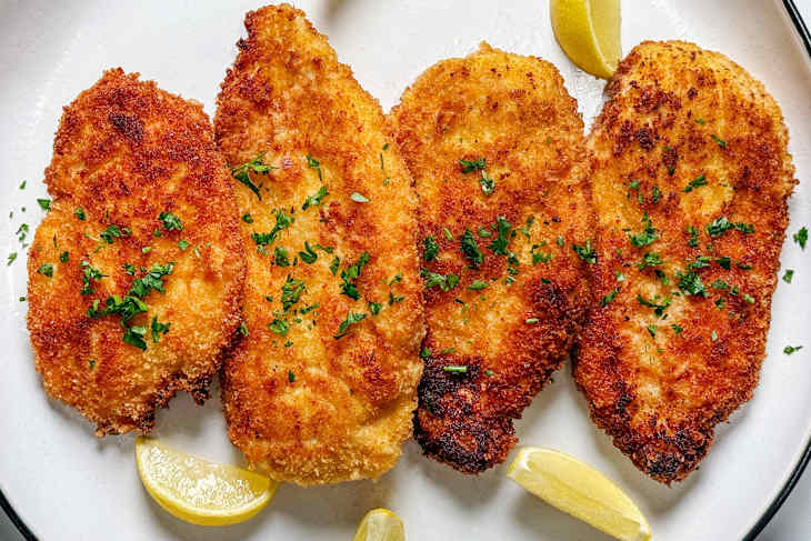 Crispy breaded fish fillets garnished with parsley and lemon wedges on a white plate.