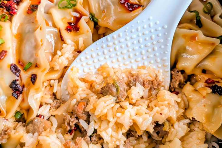 A close-up of a bowl containing dumplings drizzled with sauce and a serving of rice mixed with ground meat and herbs.