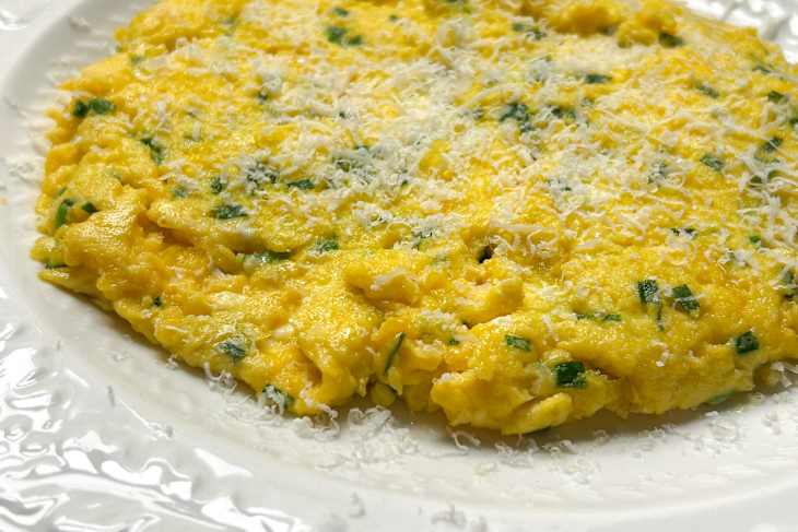 Creamy scrambled eggs with chives, topped with grated cheese, served on a decorative white plate.