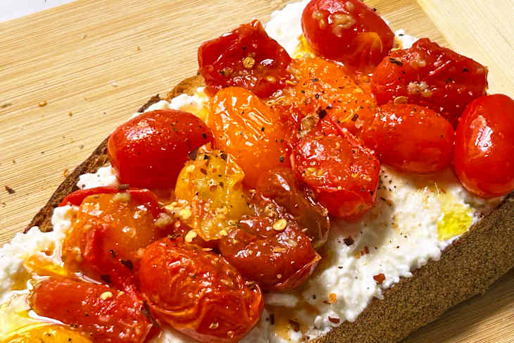 Toasted bread topped with creamy ricotta cheese and roasted cherry tomatoes, drizzled with olive oil and spices.