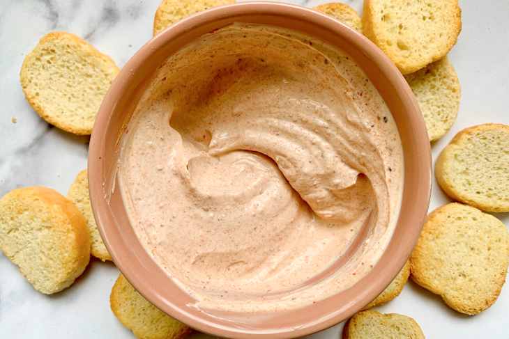 Creamy dip being scooped with a toasted bread slice.