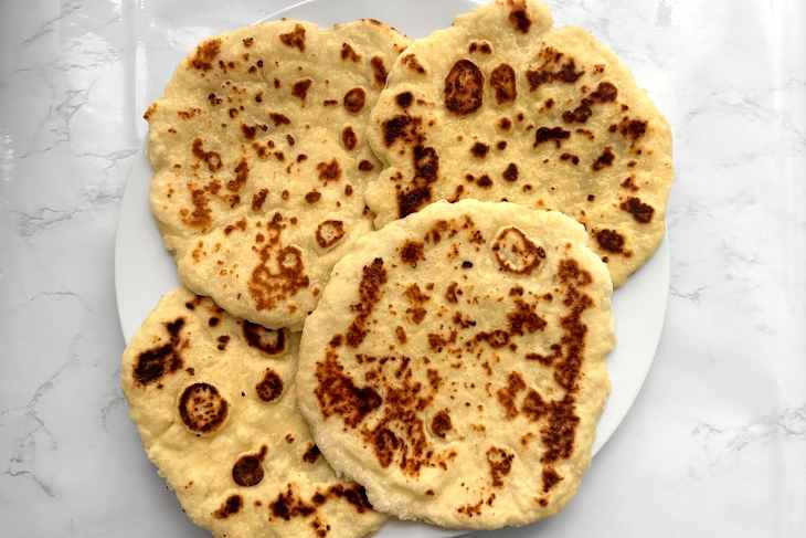 Flatbreads stacked on a white plate, showcasing golden-brown spots on a marble surface.