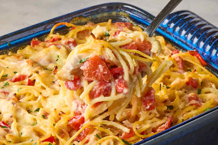 Chicken spaghetti casserole with red bell peppers and melted cheese in a blue dish.
