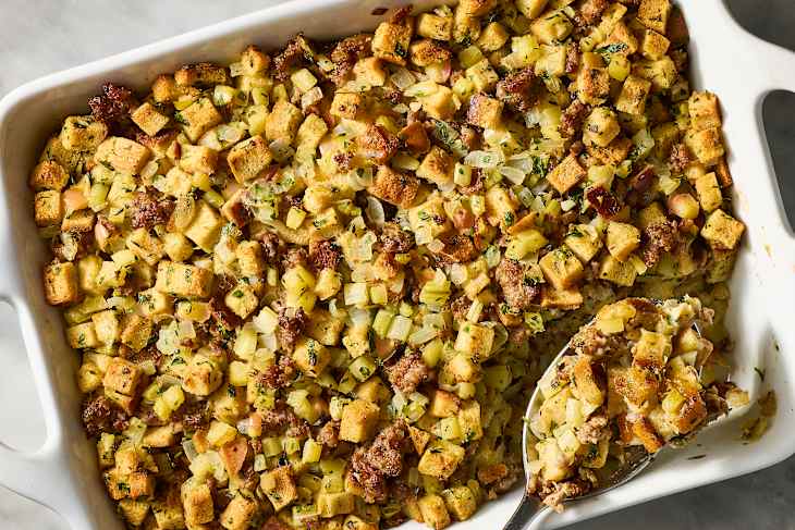 Savory stuffing with golden bread cubes, sausage, celery, and onions baked in a white dish.