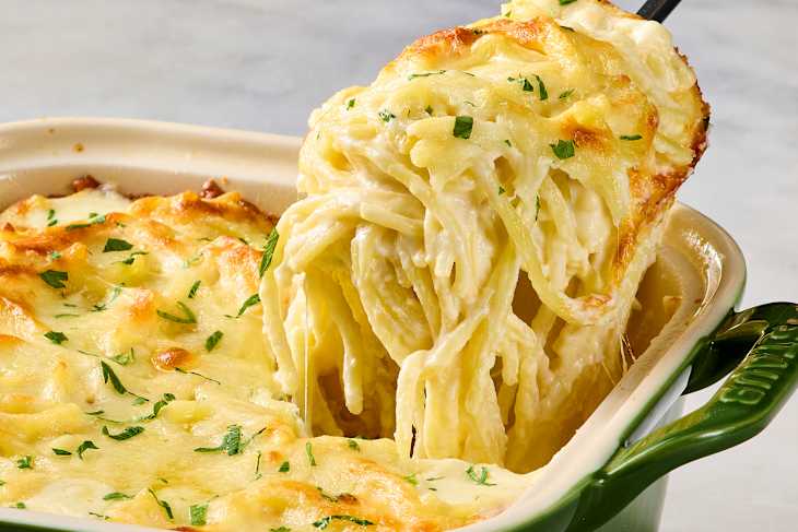 Creamy baked pasta with melted cheese and parsley, being served from a green dish.