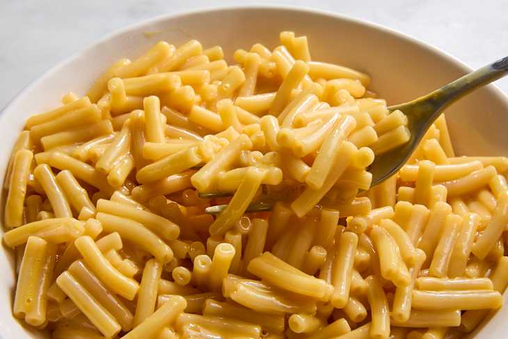 Creamy macaroni and cheese in a white bowl with a fork, featuring short elbow pasta coated in cheese sauce.