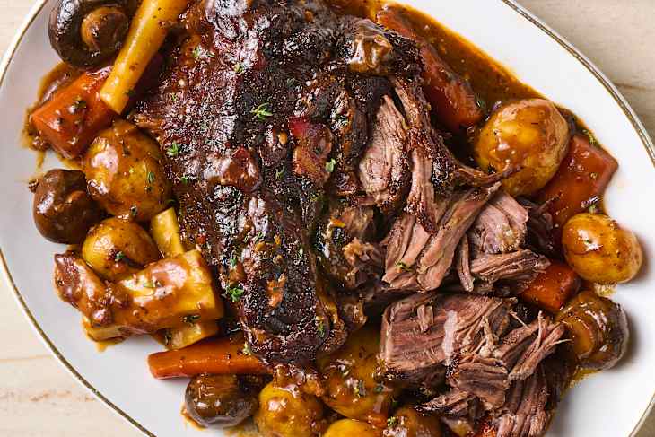 Tender pot roast with carrots, potatoes, and mushrooms in a rich gravy, garnished with fresh herbs.