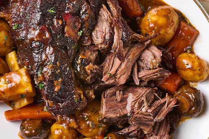 Tender pot roast with carrots, potatoes, and mushrooms in a rich gravy, garnished with fresh herbs.