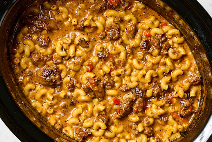 Creamy macaroni and cheese with beef, garnished with parsley, in a black slow cooker.