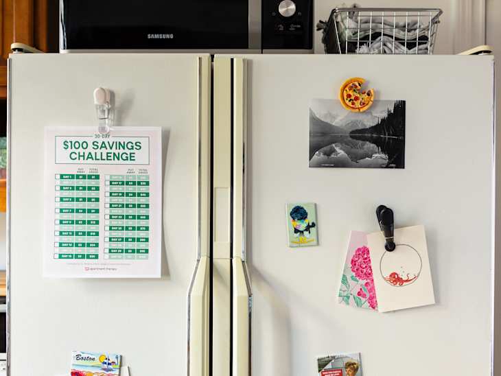 Refrigerator with $100 savings challenge chart, postcards, and magnets, including a pizza slice magnet and a Boston postcard.