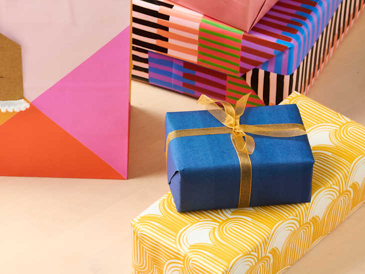 Colorful wrapped gifts stacked together, featuring a blue box with a gold ribbon on a yellow patterned box.