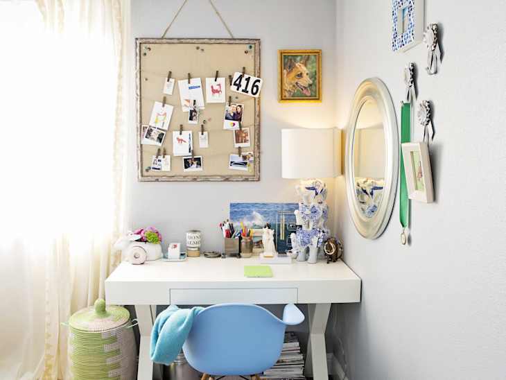 Home office with a white desk, blue chair, bulletin board with photos, and decorative items on the wall.