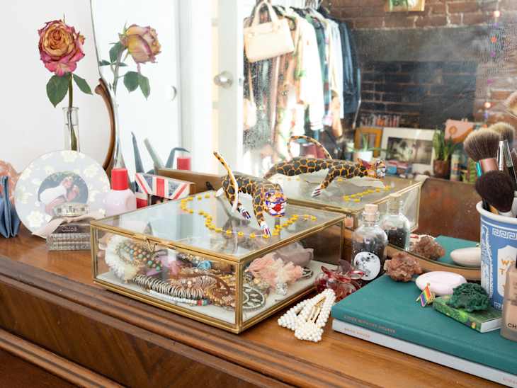 Dresser with jewelry box, makeup brushes, dried roses, and decorative items in front of a mirror.
