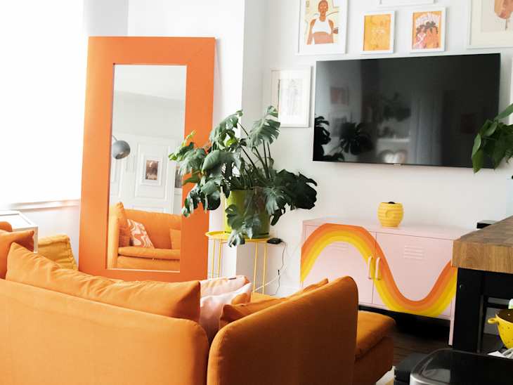 White living room with orange sofa, orange mirror, and retro paint details