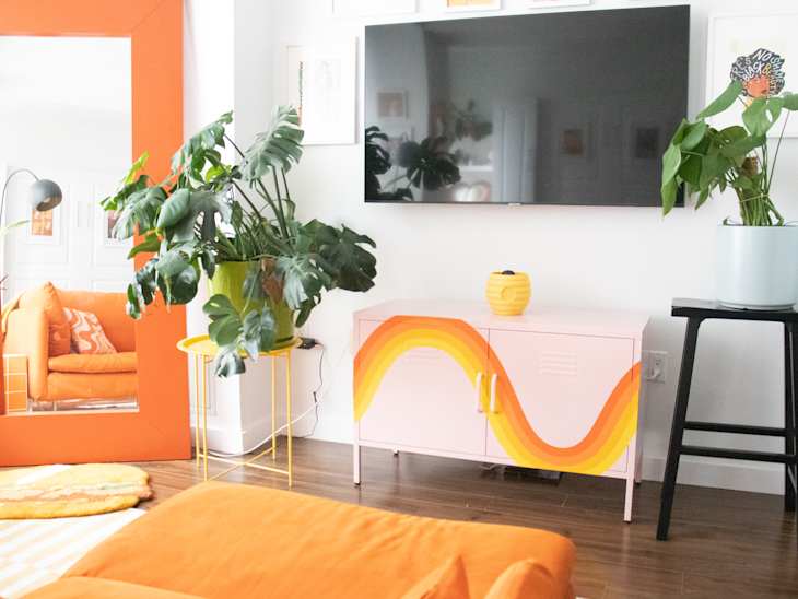 Living room with orange sofa, large mirror, pink cabinet with orange wave design, and potted plants.