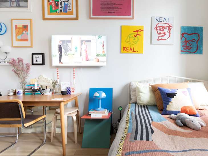 Colorful artwork hung on bedroom wall in studio apartment with colorful neatly made bed.