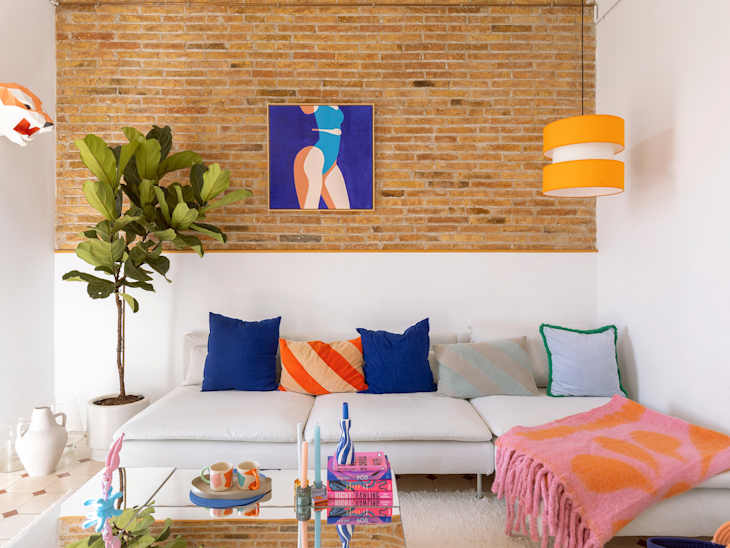 Living room with brick wall, framed artwork, and white couch with decorative pillows.