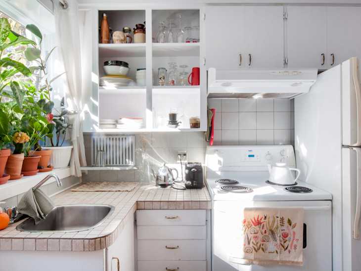 Small kitchen with white cabinets, potted plants on windowsill, and a stove with a floral towel hanging.