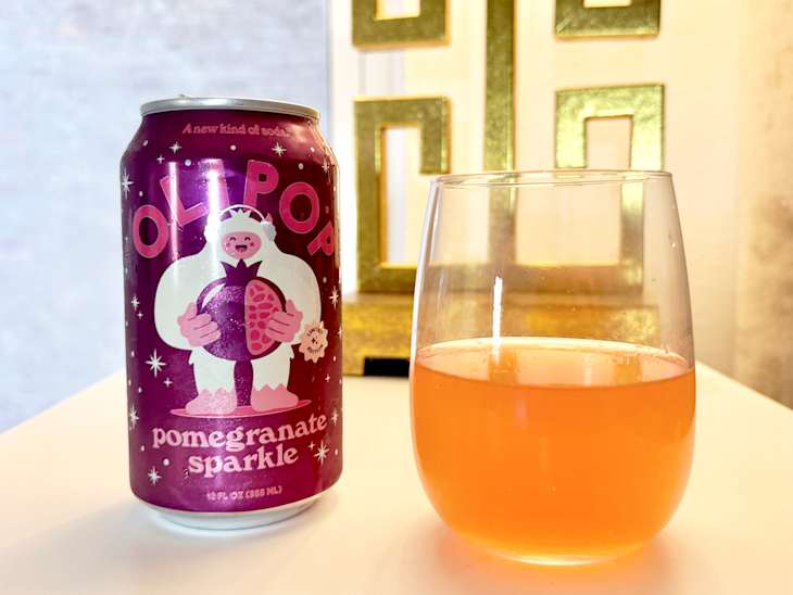 A can of OLIPOP Pomegranate Sparkle soda next to a glass of the drink, with a decorative gold background.
