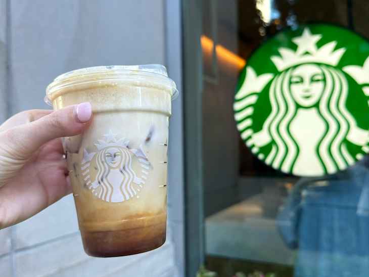 Someone holding a Starbucks Apple Crisp Shaken Espresso in front of Starbucks