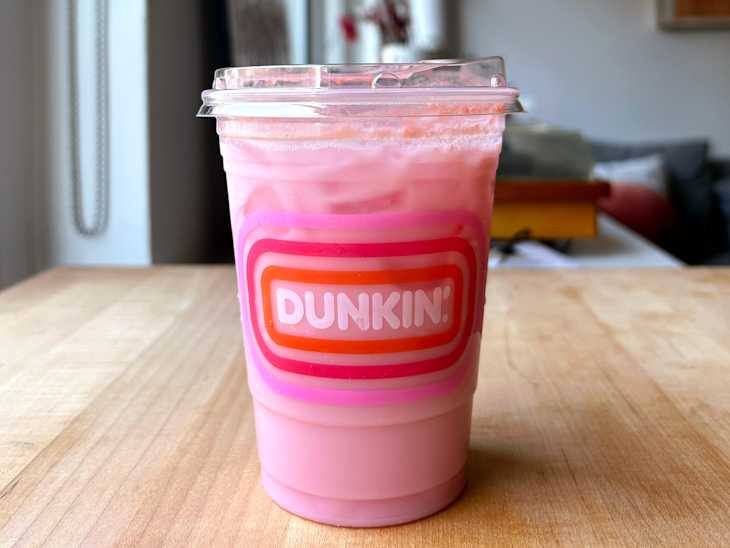 Iced pink beverage in a clear cup with a pink and orange Dunkin' logo, placed on a wooden table.