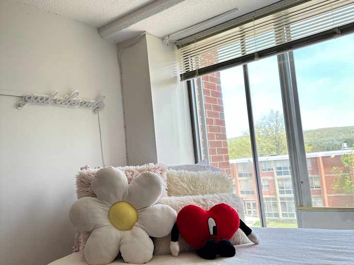 bed in dorm room with large window, white bedding, flower pillow and other decorative throw pillow