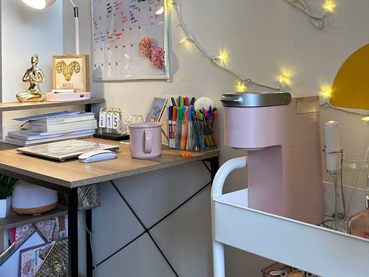 desk/table area in dorm room with small white lamp, string lights, art, calendar, white caddy/cart