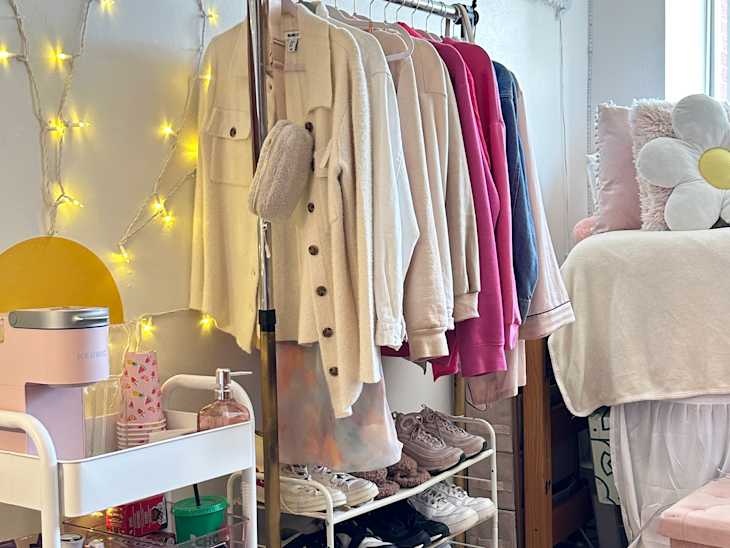 dorm room with white, pink accents, combined clothing and shoe rack, string lights, window