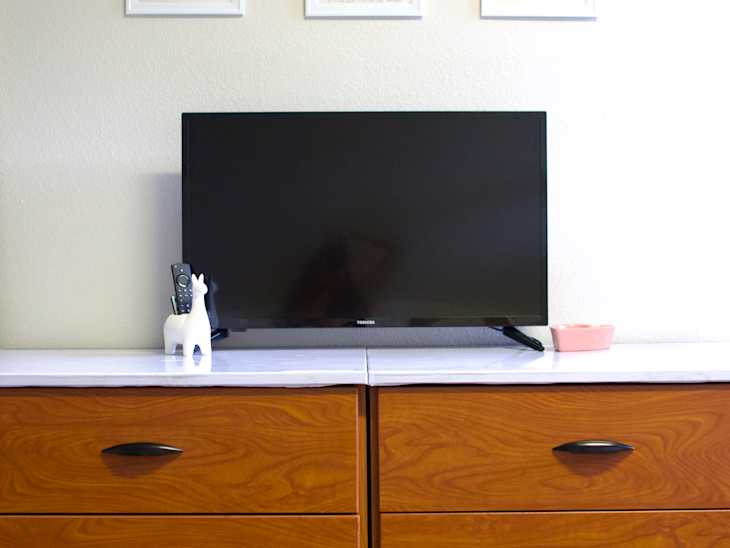 White-painted dorm room with three pieces of art hung on the wall above a large tv.