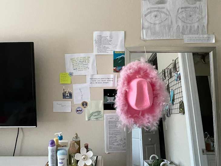 detail of dresser next to full length mirror in dorm room. Pink feather trim cowboy hat hanging on mirror. TV on the dresser